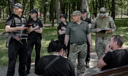 Pimakhov, Pikhota and police officers stand in front of a couple sitting on a bench