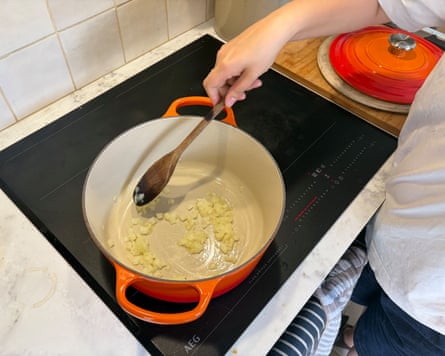 Closeup view, from above, of Sophie Wyburd testing a Volcanic colour Le Creuset casserole dish on a hob in a kitchen.