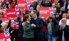 Keir Starmer and Claire Ward hug, clutching a microphone, in front of a crowd holding "Britain's Future" signs