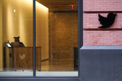 A view from the outside of a building shows a Twitter logo on the outside. Through a window, a woman can be seen working at a desk.