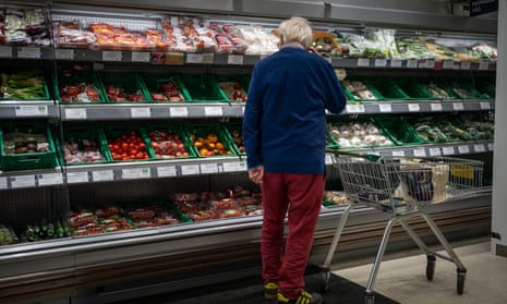 A man stands in front of the fruit and veg in a supermarket.