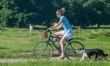 Woman cycling through park with dog.