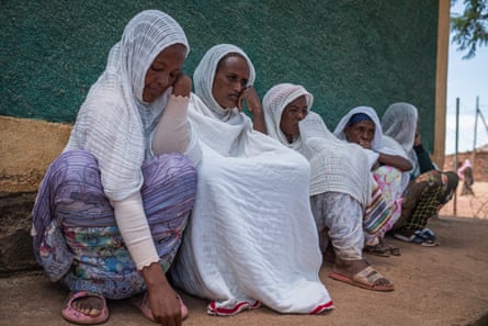 Five women with their heads covered by white scarfs sit in a row