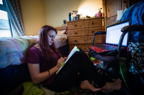 A young woman university student working on her laptop computer in her messy bedroom at home UK