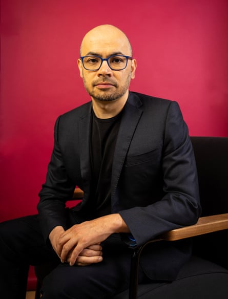 Demis Hassabis sitting, with red background behind him.