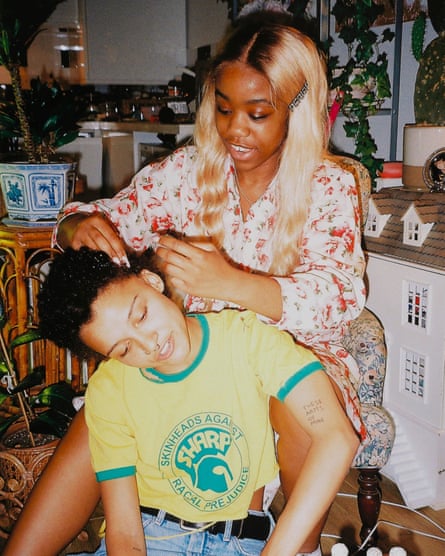 A photograph by Rene Matic titled, ‘Chiddy Doing Rene’s hair’, showing a young black woman seated behind another doing her hair