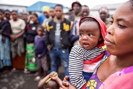 A woman holds a baby as a crowd looks on