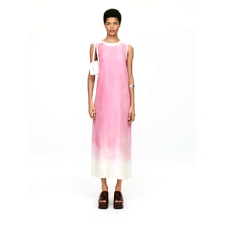 A model wear an Arket silk dress. It is a long pink sleeveless dress with ombre edges. The model also wears black open toed shoes and has a small white handbag under their right arm.