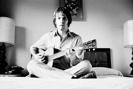 black and white photo of a man sitting on a bed with a guitar