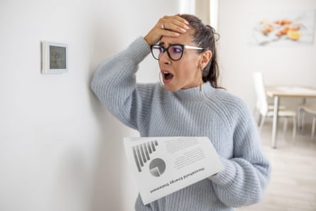 a woman slaps her forehead in despair while looking at the central heating thermostat and clutching an energy bills