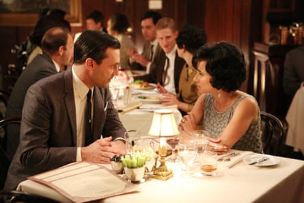 Jon Hamm and Linda Cardellini lean in close, talking intently at a restaurant table in Mad Men