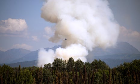A helicopter passes by as smoke rises from a wildfire on 3 July south of Talkeetna, Alaska. 
