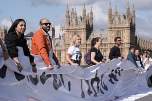People stand on a bridge with a banner and the Houses of Parliament in the background
