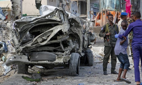 Security forces stand near the wreckage of an official vehicle destroyed in the first of Saturday’s bomb attacks, in Mogadishu.
