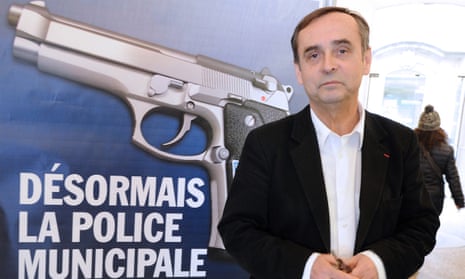 Robert Ménard poses in front of a municipality campaign poster showing a handgun