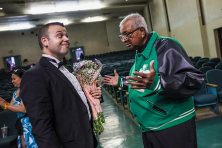 Man in tux speaks with man in green bomber jacket.