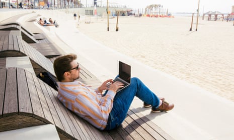 A man types on his laptop on a beach in Tel Aviv.