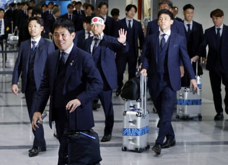 The team, wearing blue suits, push their wheeled suitcases through the airport