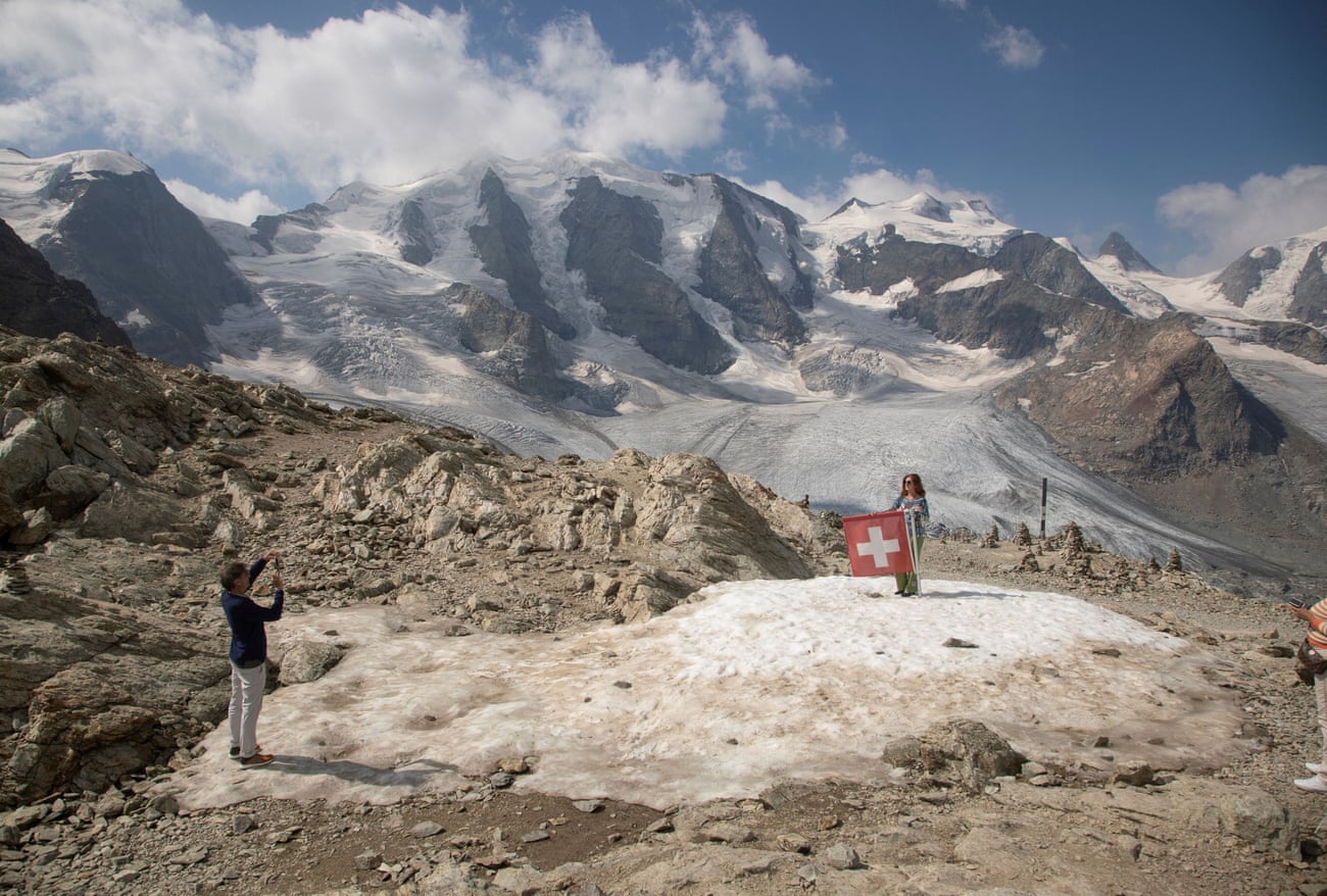 A woman poses beside a Swiss national flag near Mount Piz Palue