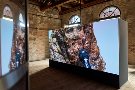 The face of an anthropomorphic excrement talks into a microphone on a video screen inside the pavilion