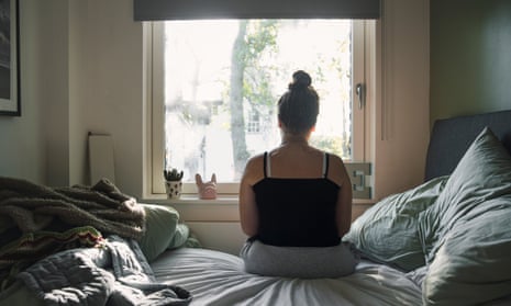 Rear view of a teenage girl looking out of the window whilst sitting on her bed