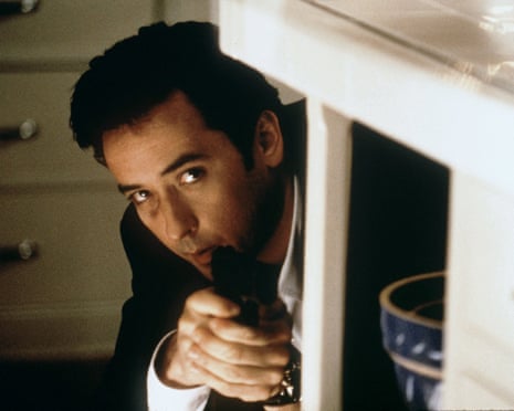 John Cusack, in a suit, levels a revolver while crouching under a table