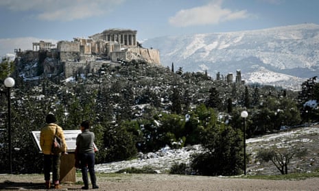 Women look at an information board at the Pnyx hill in central Athens, while the remains of heavy snowall cover the Acropolis and nearby hills in Athens on February 17, 2021.