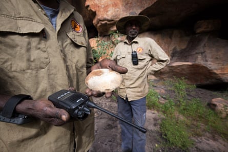 Indigenous ranger Berribob Watson holds modern and ancient technology, a two-way radio and a stone used for grinding pigments for painting. Warddeken ranger Ricky Nabarlambarl stands behind.