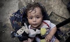 A Palestinian baby holding a soft toy looking up at the camera
