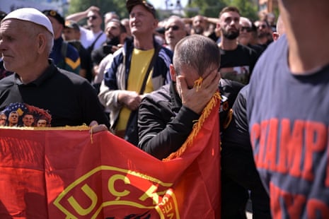 A man stood among demonstrators covers his face with his hand.