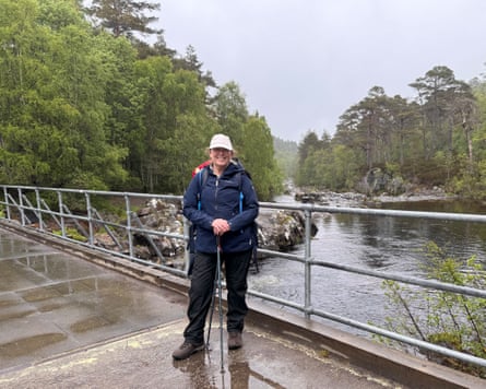Female hiker with walking poles on a bridge over a river on a wet day