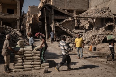Day labourers carry sacks of cement for mixing at a construction site next to destroyed buildings
