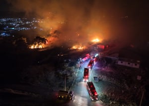An aerial photograph of a row of firefighters' trucks next to a wildfire