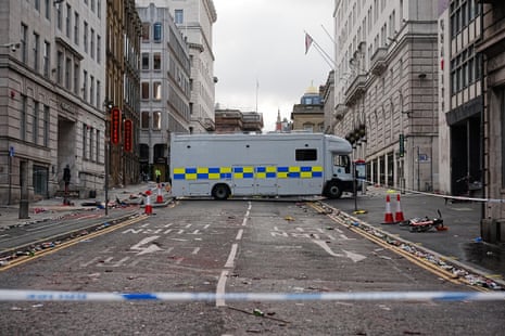 A police van parked in the middle of the road, with police tape visible in the foreground.