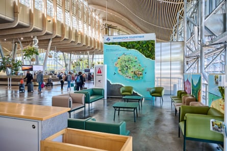 Passengers walk past a seating area in the airport, which has a large map of Réunion displayed alongside