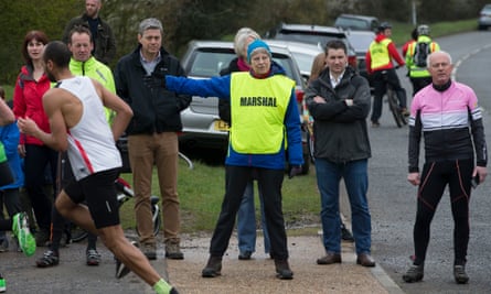 Theresa May wearing a hi-vis marshal's vest points the way for runners
