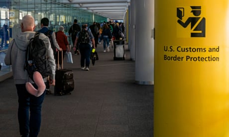 travelers walk past a yellow pole that reads 'US customs and border protection'
