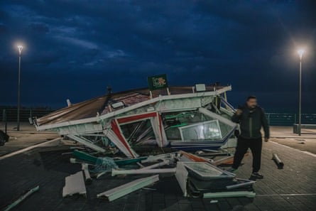 A man stands alongside a destroyed kiosk bar at night