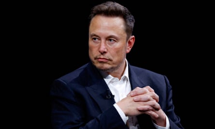 Elon Musk looking serious with his hands clasped in front of him
