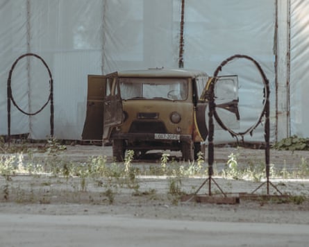 A rusty old car sits near metal hoops mounted on stands