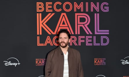 Actor Daniel Brühl poses in front of a colorful 'Becoming Karl Lagerfeld' sign.