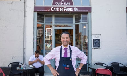 He stands in front of a sign that says Cafe de Paris