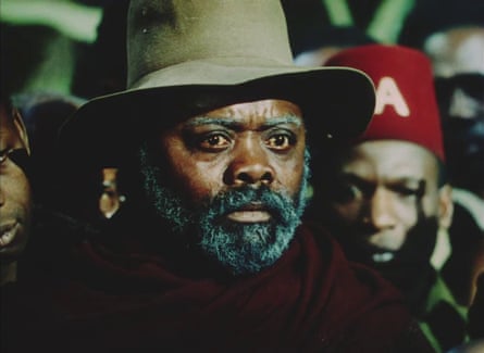 A close up of a sombre or anxious-looking man with rich silvering beard and eyebrows wearing a deep hat
