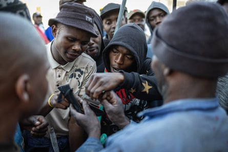 A man desperately holds out his ID card that is being inspected while others holding weapons look on