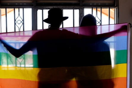 Two people in silhouette stand holding a pride flag behind them.