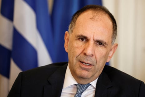 Greek foreign minister George Gerapetritis is pictured in a suit with Greek flags behind him.