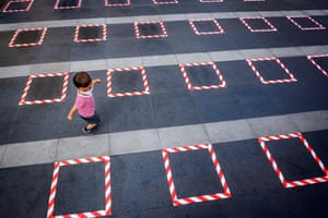 A child wearing a protective facemask runs on a sidewalk marked for social distancing in front of a Buddhist shrine in Bangkok