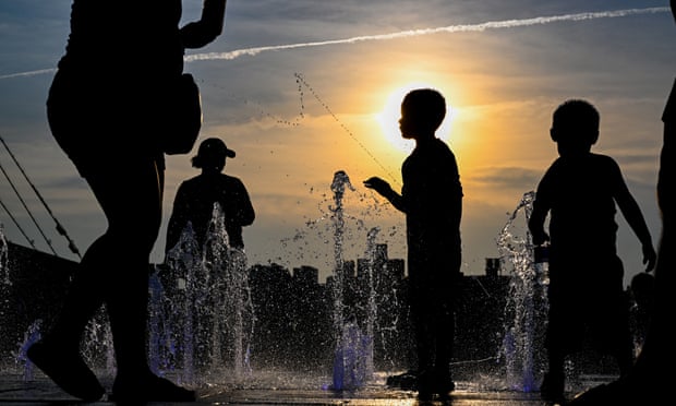 Children cool off in a fountain in Domino Park, Brooklyn with the Manhattan skyline in the background