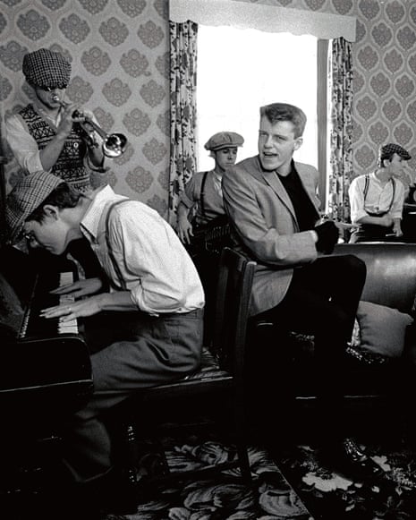 Madness band members play instruments and sing together in a wallpapered living room