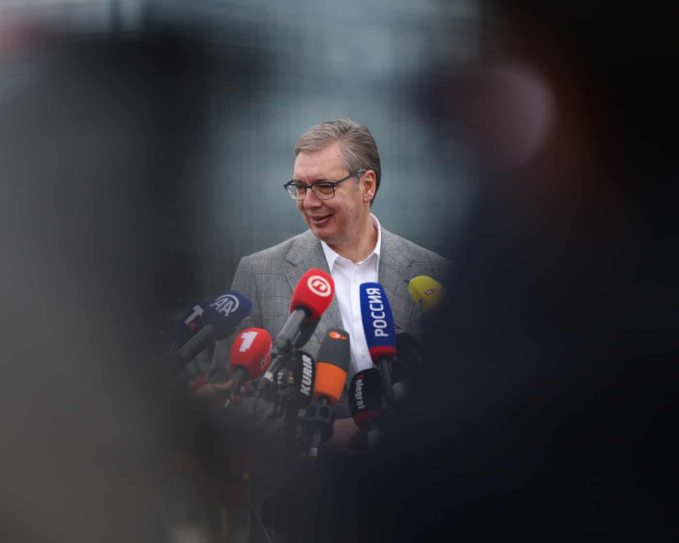 Aleksandar Vučić smiles while speaking into numerous microphones held up before him
